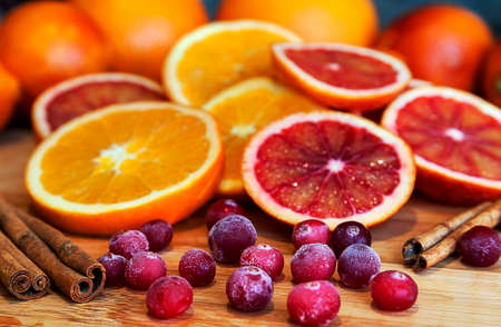 Whole and cut orange and red oranges with red cranberry and cinnamon in the foregroundの写真素材