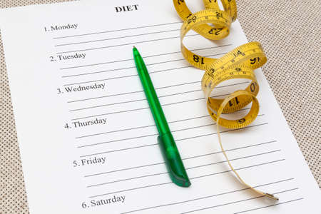 paper with blank diet plan, pen and yellow measure tape on tableの写真素材