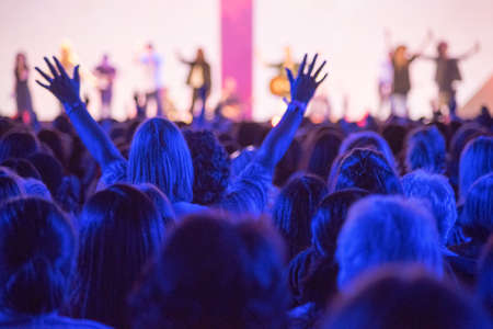 Open hands raised up in foreground with anonymous guitar player on stage in background