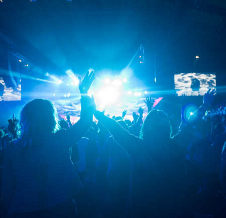 Anonymous Woman with Arms Up in Crowd of People Looking Towards Brightly LIt Stageの写真素材