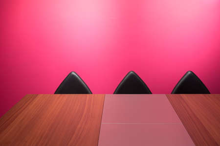 Bright Pink Office Space with Large Wooden Desk and Artistic Angular Black Leather Chairの写真素材