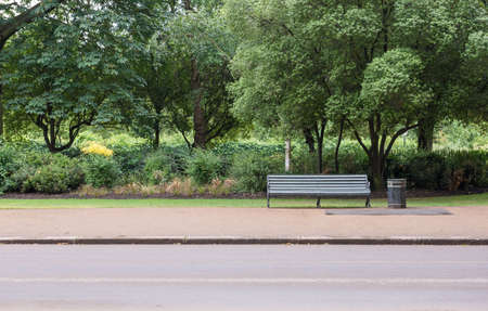 Traditional Park Bench with Litter Trash Bin in Green park with Pavement Sidewalkの写真素材