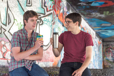 Two Casual Young Adults Drinking Coffee and Chatting in Graffiti Skate Parkのeditorial素材