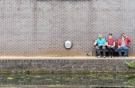 Three Male Friends Drinking Coffee and Enjoying Sitting Near Canal Riversideの写真素材