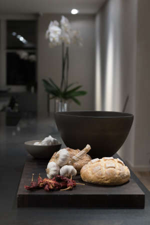 Loaves of Crusty Bread on Dark Wooden Chopping Board with Cloves of Garlic and Chilliesの写真素材