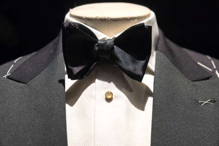 Close up on top part of tailored jacket on mannikin with black bow tie and sequined buttons on shirt