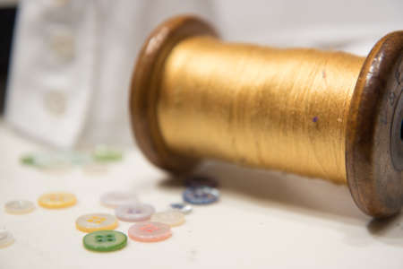 Wooden Spool with Yellow Threas with Assorted Buttons and White Shirt Cuffの写真素材