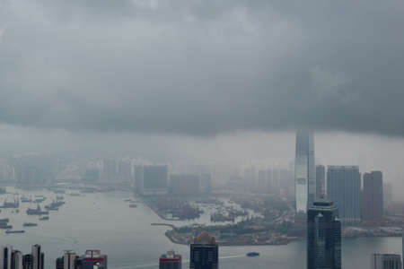 High modern buildings and boats in fog and thick rain clouds of Hong Kong harbor from view pointの写真素材