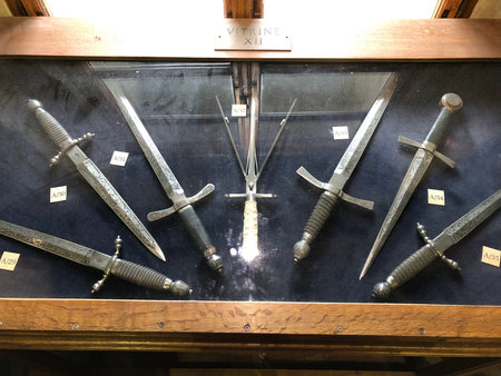 Swords are displayed in a wooden-framed glass case at a museum in Golden Lane, Prague