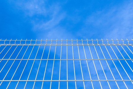 white industrial fence making patterns looking to the blue skyの写真素材