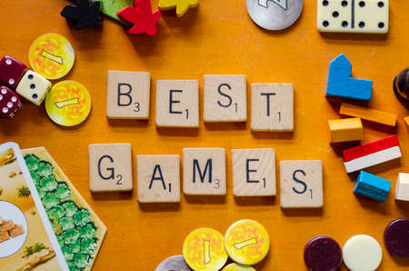 Quito, Picincha / Ecuador; November, 23, 2021. "best games" spelled out in wooden letter tiles. Surrounded by dice, dominoe pieces, settlers of catan and carcassone pieces, on a wooden background.のeditorial素材