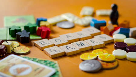 Quito, Ecuador; November, 23, 2021. "Board games" spelled out in scrabble tiles, Surrounded by dice, dominoe pieces, settlers of catan and carcassonne pieces, on a wooden background.のeditorial素材