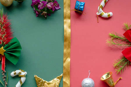 christmas decor background, on red and green paper it is divided by a golden ribbon, there are ribbons canes and a present and a bell. some plants.の写真素材