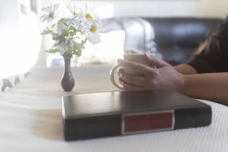 Woman taking a cup of coffee and a book on the tableの写真素材