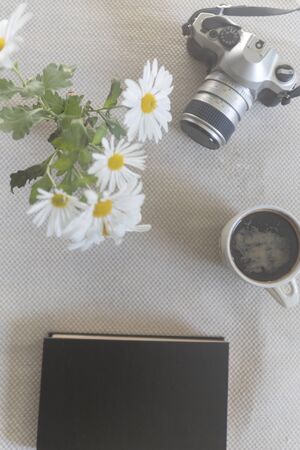 Background table with reflex camera, a cup of coffee, black book and flowers, wich are daisiesの写真素材