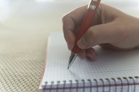Young girl hand writing with a red pen on a empty notebook. 