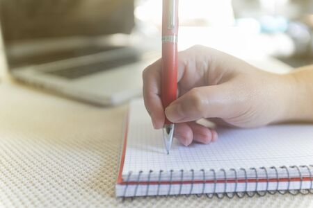 Young woman writting on notebook on table with a laptop during a sunny day indoorの写真素材