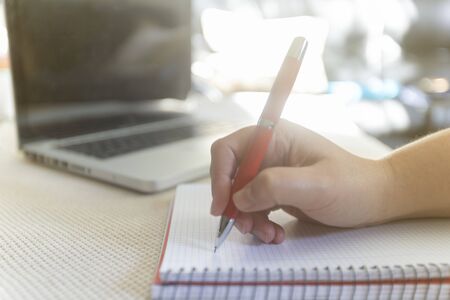 Young woman writting on notebook on table with a laptop during a sunny day indoorの写真素材