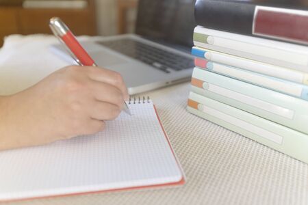 Young woman writting on notebook on table with a laptop during a sunny day indoorの写真素材