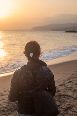 Photography of young and white woman looking at the sea during the sunset, with a braid and coat, during the winter.の写真素材