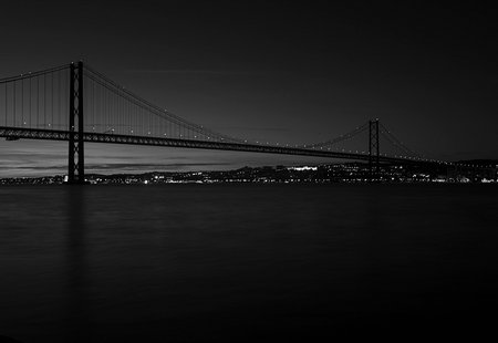 Black and white photography of the 25th April bridge in Lisbon during the night, over the Tagus River and skyline of the city of Lisbon. Views from Cacilhasの写真素材