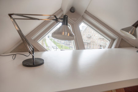 Photograph of the Kubuswoning, the cube houses in Rotterdam, The Netherlands. Yellow color and original architecture. Detail of the interior of one of the apartments room with a white desk and flexo lamp and window with views to the cityの写真素材