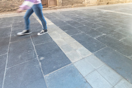 Photograph that captures the detail of the legs and shoe of a young girl walking through the city. Black sports shoes, casual style and jeans.の写真素材