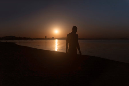 An inspiring silhouette of a young, strong man standing on the sandy beach at La Manga del Mar...