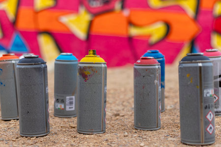 Close-up of spray paint cans with splashes of vibrant paint, resting in front of a striking graffiti mural on a wall. A vivid scene capturing the artistry and tools of street art culture.の写真素材