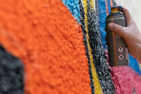 Close-up of a hand gripping a spray paint can, actively painting a vibrant graffiti design on a wall. The dynamic scene captures the energy and creativity of street art in action.の写真素材