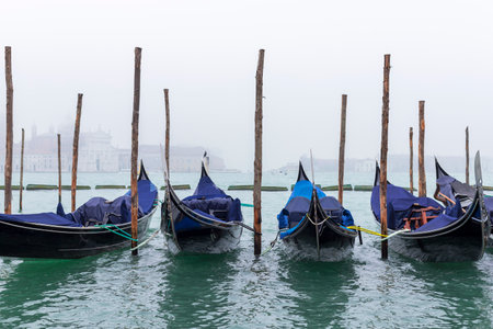 A captivating close-up of gondolas gently moored in the Venetian lagoon on a foggy day. The mist shrouds the background, creating an atmospheric and timeless view of Venice's iconic waterways.の写真素材