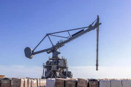 Dynamic image of a crane operating at a busy port, lifting and moving cargo packages. The scene highlights the industrial labor and logistics involved in maritime transport and trade. With strong lines and a functional atmosphere, the photo reflects the coordination, strength, and precision required in port operations. Perfect for illustrating concepts like shipping, freight logistics, heavy machinery, and blue-collar professions.の写真素材