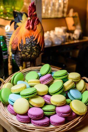 Multicolored macaroon in a wicker basket on the table with a figure of a roosterの写真素材