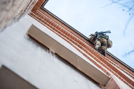 Soldier with a gun on the edge of the roof coming down on a ropeの写真素材
