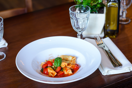 Italian dish of pasta and tomato served on a wooden table in a restaurantの写真素材