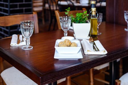Dish of potato balls, cutlery, napkins and wine glasses on a wooden table in a restaurantの写真素材
