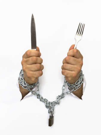 man hands handcuffed with chains holding knife and a fork