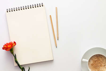 White table at home. Open empty sketchbook, wooden pencils and an orange-red carnation. Cocoa with foam in a white cup. Mockup. Creative deskの写真素材