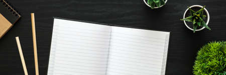 A black desk with an open notebook, plants and office supplies. Panoramic photoの写真素材
