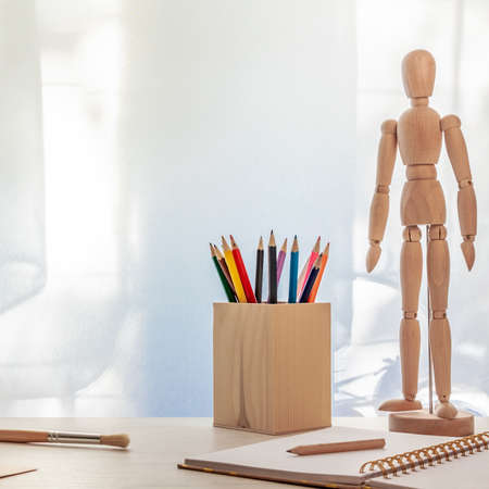 Photo with an open notebook, brush, wooden puppet and pencils on the background of a window with a curtainの写真素材