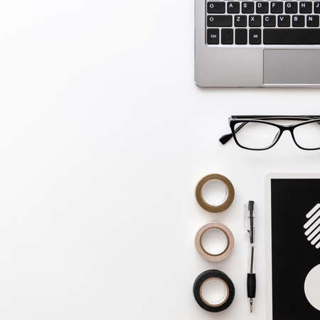 White desk copy space seen from above with a laptop keyboard, a pen, glasses, a notebook with wheels...