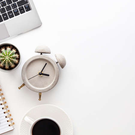 White desk copy space seen from above with a laptop keyboard, notebook, coffee, gray concrete clock...