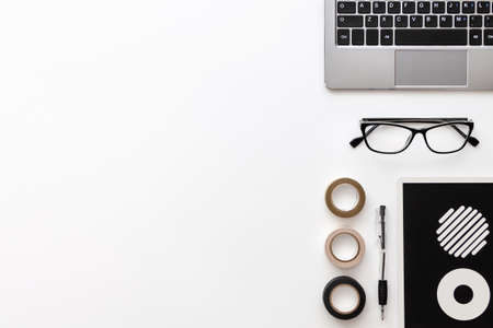 White desk copy space seen from above with a laptop keyboard, a pen, glasses, a notebook with wheels and three tapesの写真素材