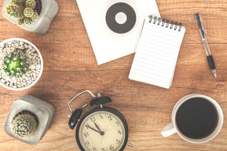 Top view on wooden desk with notebook, cup of coffee, cactuses, clock and penの写真素材