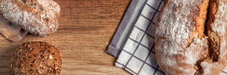Panoramic view on wooden table with bread and rolls on checkered material and old paperの写真素材