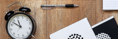 Panoramic view on wooden desk with a black cloc and notebook in circles 