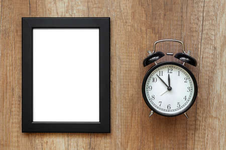 Wooden desk with black clock and empty black frameの写真素材