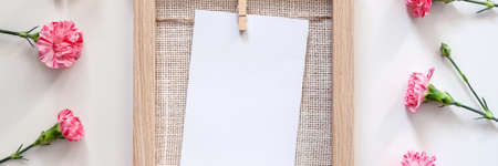 A panoramic photo of a wooden mockup frame with a natural jute filling with pink flowers located on a white deskの写真素材