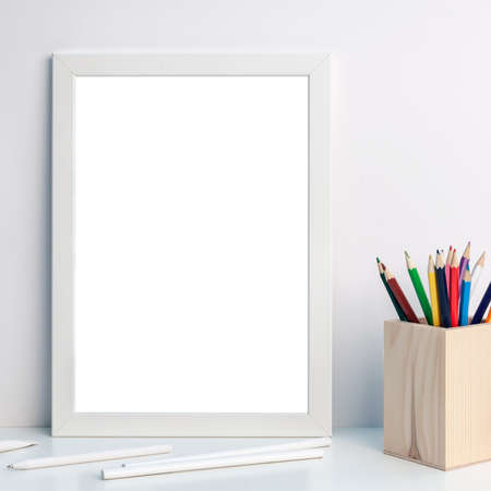 Photo of a white mockup frame with colorful pencils in a wooden toolbox on a desk