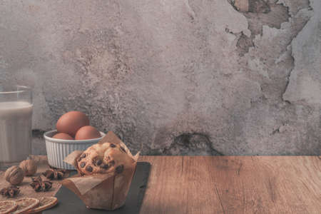 Brown wooden table on a background of empty concrete wall with glass of milk, chocolate muffin,...
